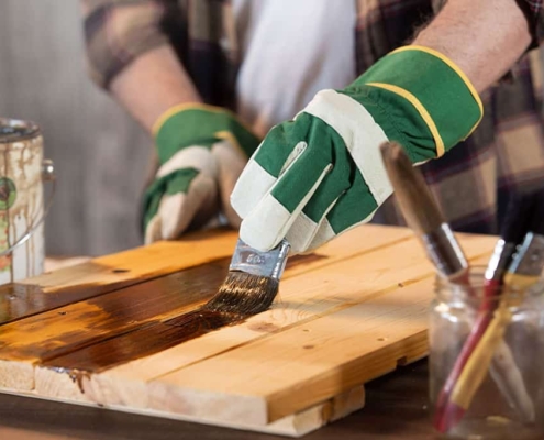 Ökologischer Holzschutz im Einsatz – Lasur für den Außenbereich Handwerker streicht Holz mit natürlicher Holzlasur – nachhaltiger Holzschutz außen mit Pinsel