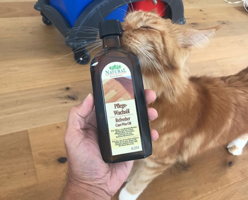 Haustierfreundliche Holzpflege – natürliches Wachsöl für geschützte Oberflächen Katze schnuppert an einer Flasche Natural Pflege-Wachsöl auf einem Holzboden